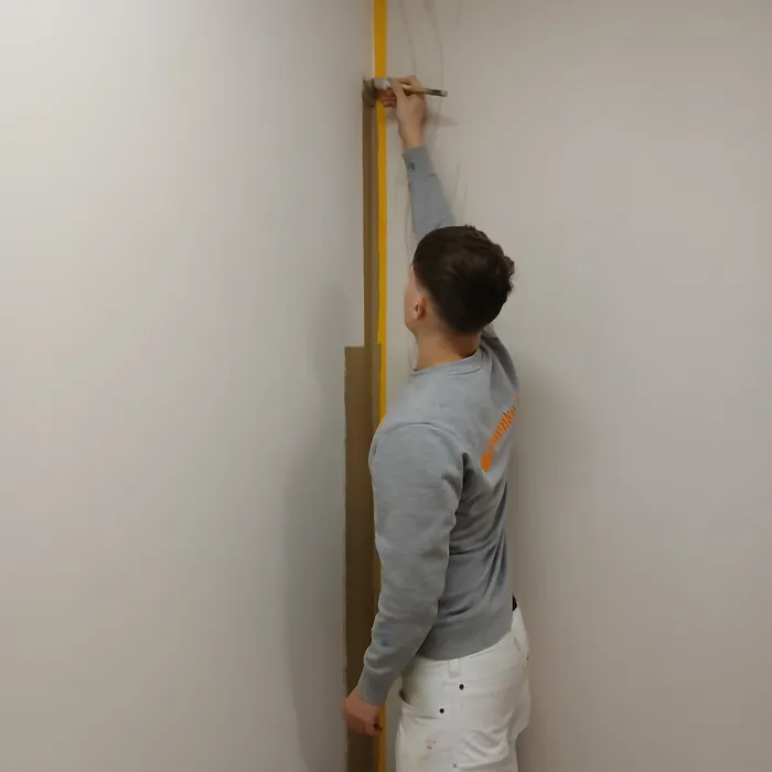 Schilder van Bonke & Zn. snijdt strak langs het plafond tijdens binnenschilderwerk in een zorgomgeving op de SEH in Enschede.