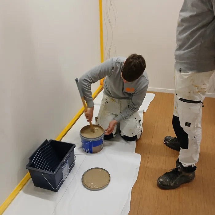 Leerling mengt Sigma Pearl Clean Matt verf in RAL 1019 voor schilderwerk in de afscheidskamer van Medisch Spectrum Twente in Enschede.