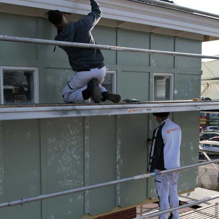 Twee schilders van Bonke & Zn. werken aan kozijnen en dakoverstek van de watertoren op de steiger