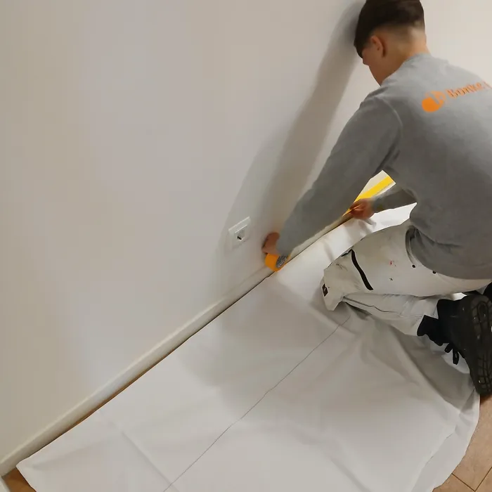 Leerling van Schildersbedrijf Bonke & Zn. plakt plinten af en dekt de vloer af tijdens voorbereiding van schilderwerk in de afscheidskamer op de SEH in Enschede.