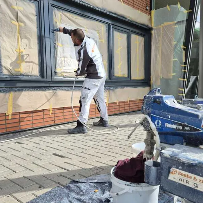 Medewerker van Bonke & Zn. spuit kozijnen, ramen afgeplakt ter bescherming