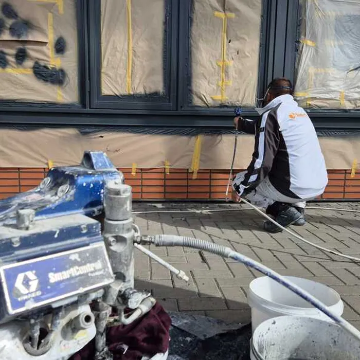Medewerker van Bonke & Zn. hurkt bij afwerking kozijn onderaan de gevel